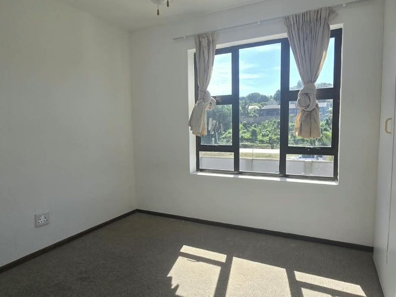 A bright, empty bedroom featuring built-in cupboards, carpeted flooring, and a large window providing natural light.