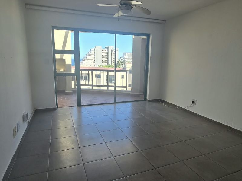 An empty living room featuring tiled flooring, a ceiling fan, and a large sliding glass door that opens onto a balcony with urban views.
