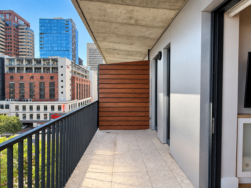 A modern, well-maintained balcony featuring tiled flooring, a timber privacy screen, and a metal balustrade with expansive urban city views.