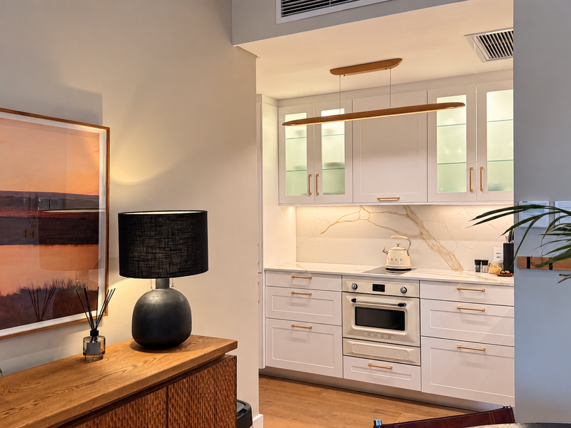 Modern kitchen featuring white cabinetry, integrated oven, cooktop, and elegant stone splashback with warm under-cabinet lighting.