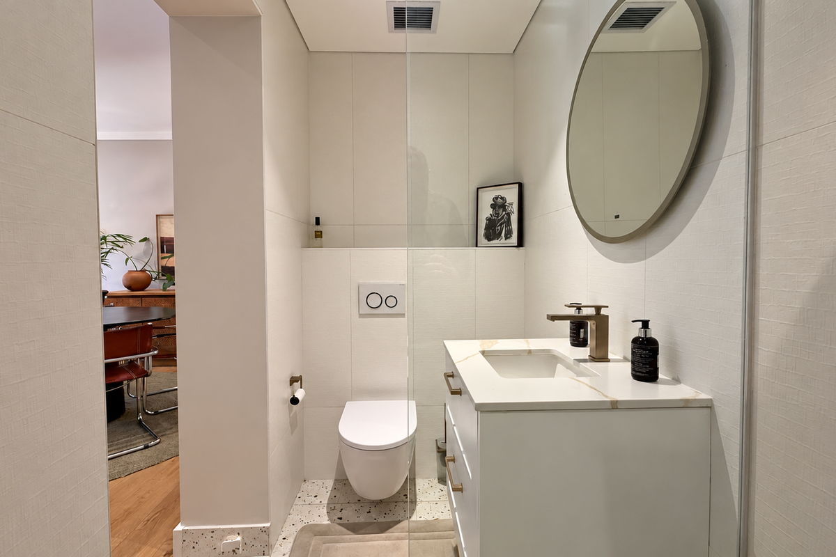 Modern bathroom featuring a wall-mounted toilet, vanity with stone countertop, brass fixtures, and stylish terrazzo flooring, presented in excellent condition.