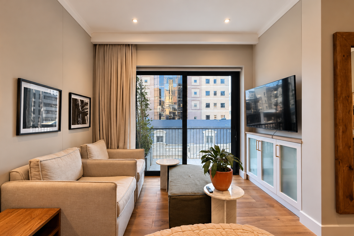 A well-maintained living room featuring hardwood flooring, built-in cabinetry, and a sliding glass door providing access to a balcony with city views.