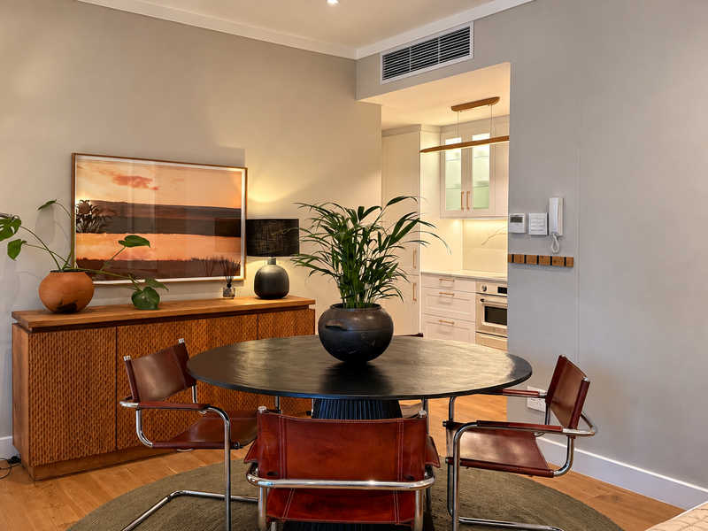 A well-maintained open-plan dining area featuring timber flooring, ducted air conditioning, and a seamless transition into a modern kitchen with built-in appliances.