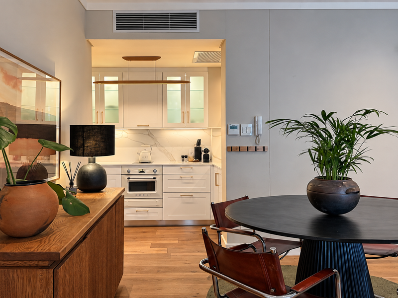 A well-appointed open-plan living and dining area featuring modern cabinetry, integrated kitchen appliances, and high-quality timber flooring with ducted air conditioning.