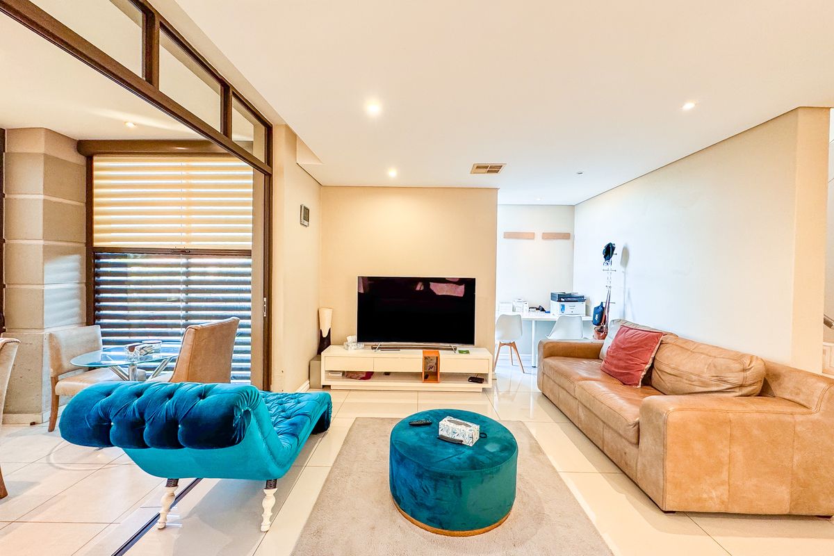 A bright and spacious living room featuring tiled flooring, recessed downlighting, and large sliding glass doors that provide access to an adjacent patio area.