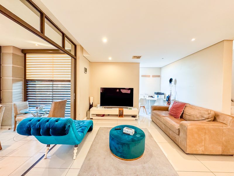 A bright and spacious living room featuring tiled flooring, recessed downlighting, and large sliding glass doors that provide access to an adjacent patio area.