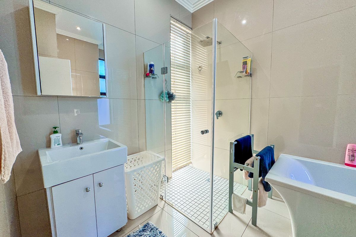 Modern bathroom featuring a vanity with basin, a glass-enclosed shower, and a freestanding bathtub with neutral wall tiling and recessed lighting.