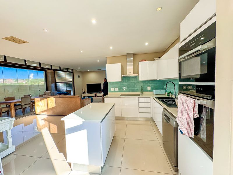 Modern open-plan kitchen featuring white cabinetry, a central island, and integrated appliances, flowing seamlessly into the adjacent living and dining area.