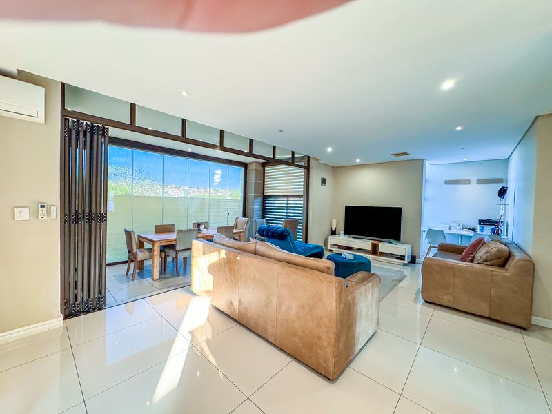 Spacious open-plan living area featuring large format floor tiles, recessed lighting, and stacking glass doors that open onto an enclosed patio space.