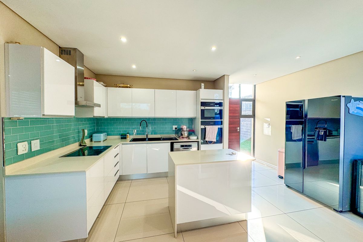 Modern kitchen featuring white high-gloss cabinetry, quartz countertops, a vibrant teal subway tile backsplash, integrated appliances, and a central island with tiled flooring.