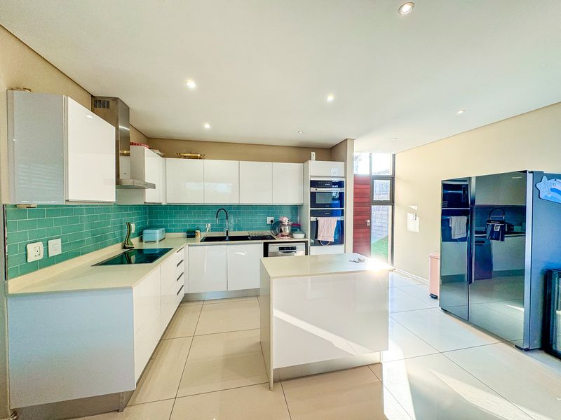Modern kitchen featuring white high-gloss cabinetry, quartz countertops, a vibrant teal subway tile backsplash, integrated appliances, and a central island with tiled flooring.