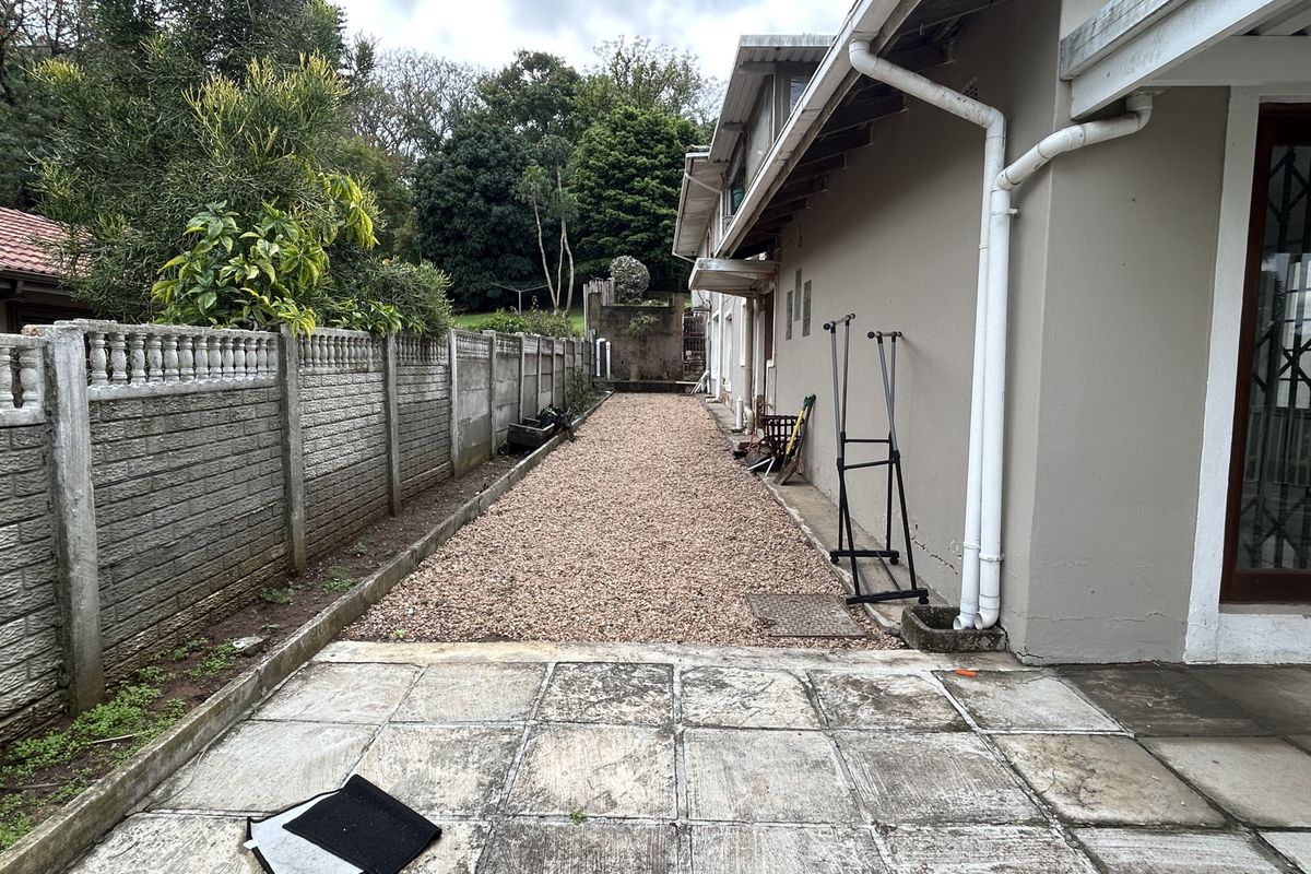 Rear exterior area featuring a gravel pathway alongside the cottage, bordered by a precast concrete wall and paved patio section.