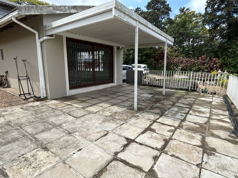 A covered outdoor patio area featuring paved flooring and direct access to the interior through a sliding glass door with security gate.