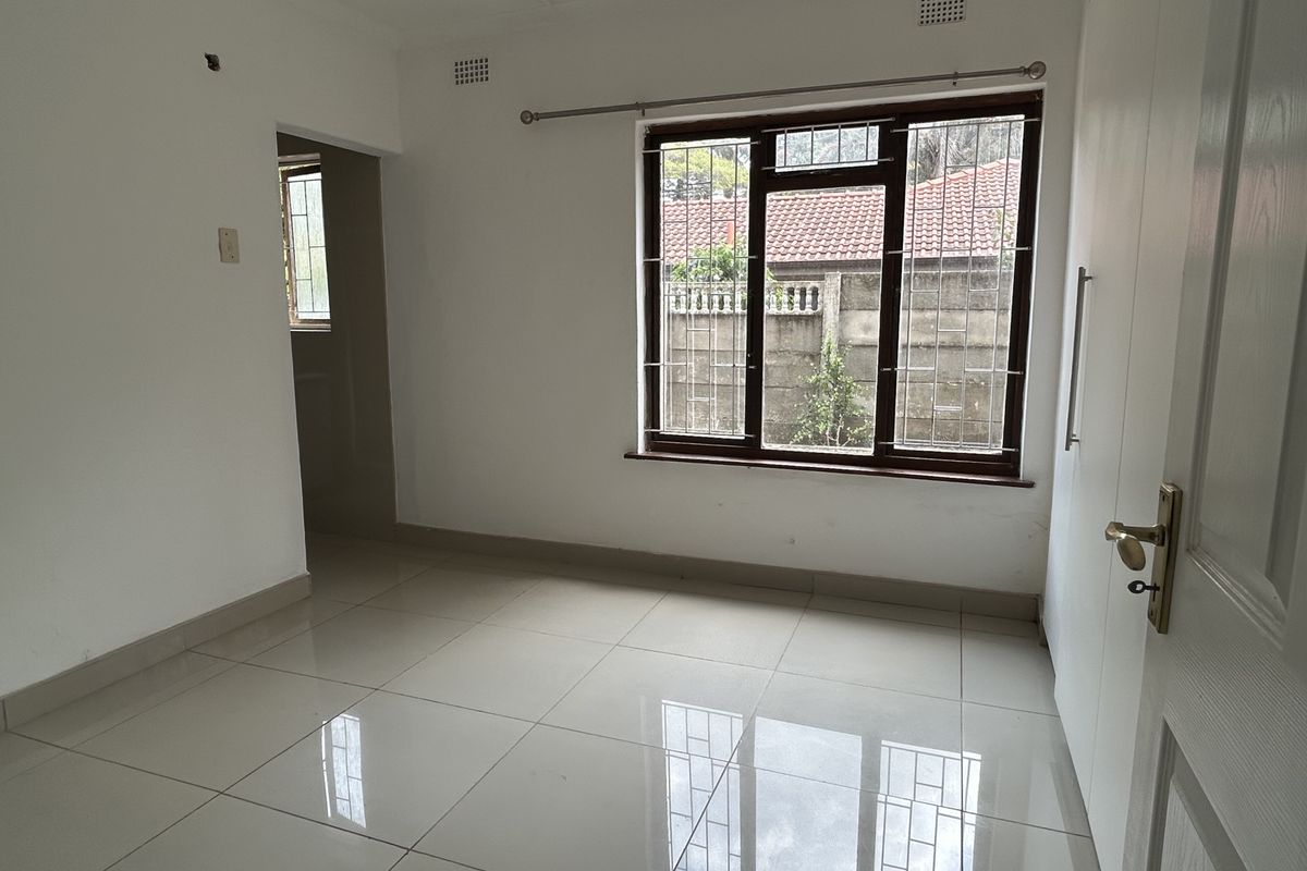A bright, empty bedroom featuring polished tiled flooring, built-in cupboards, and large windows with security bars, offering a clean canvas for personalization.