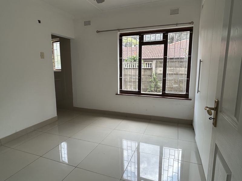 A bright, empty bedroom featuring polished tiled flooring, built-in cupboards, and large windows with security bars, offering a clean canvas for personalization.