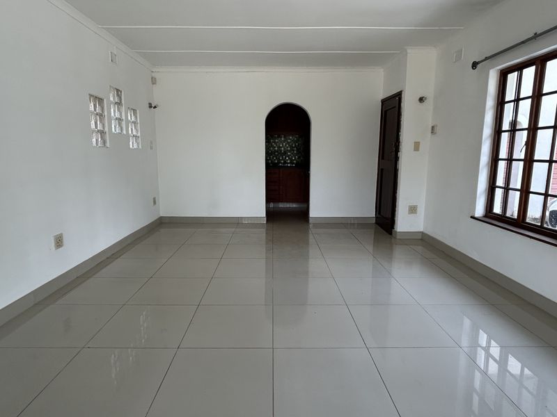 A bright, empty living room featuring neutral tiled flooring, an arched entryway, and a unique glass block feature wall.