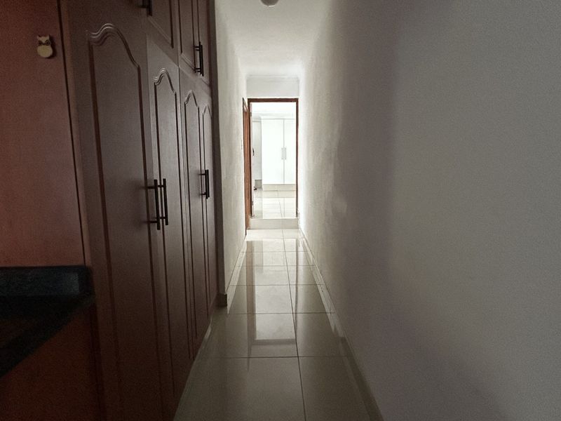 A narrow hallway featuring tiled flooring and extensive built-in cabinetry, leading towards an adjacent room.