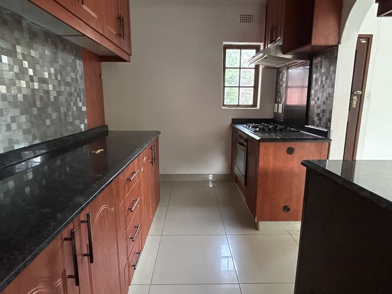 A functional kitchen featuring wooden cabinetry, granite countertops, a gas hob, built-in oven, and mosaic tile backsplash with neutral floor tiling.