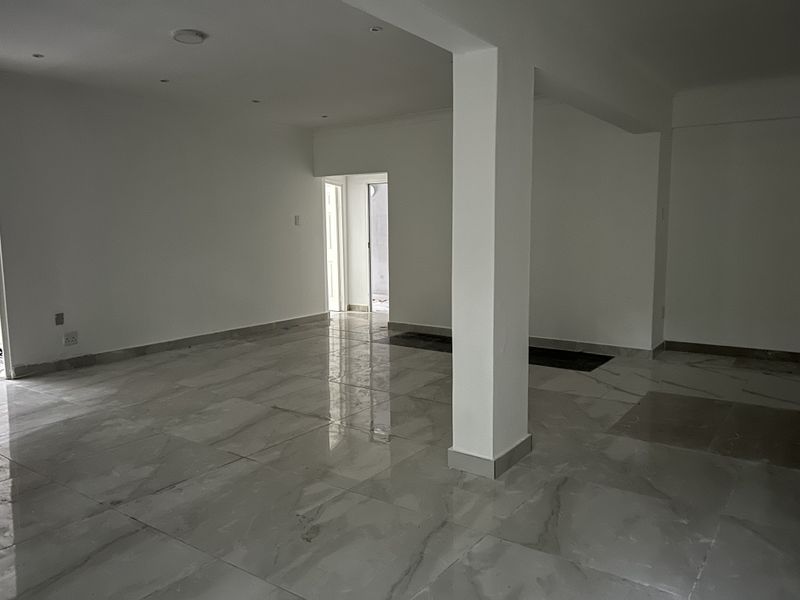 A spacious, empty open-plan living area featuring polished porcelain tile flooring, recessed lighting, and a central structural support column.