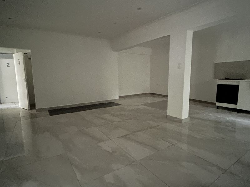 An empty open-plan living and kitchen area featuring large floor tiles, recessed lighting, and a structural pillar, awaiting interior design and furnishing.