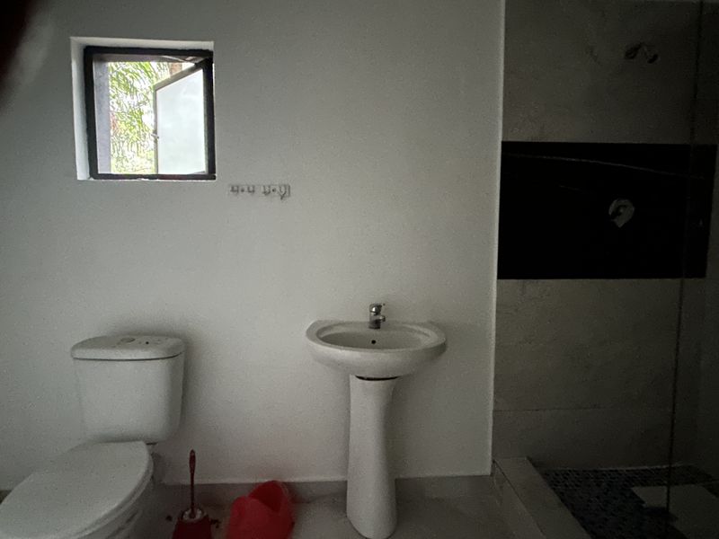 A basic bathroom featuring a pedestal basin, toilet, and shower area with tiled wall accents, currently requiring finishing touches and fixture installation.