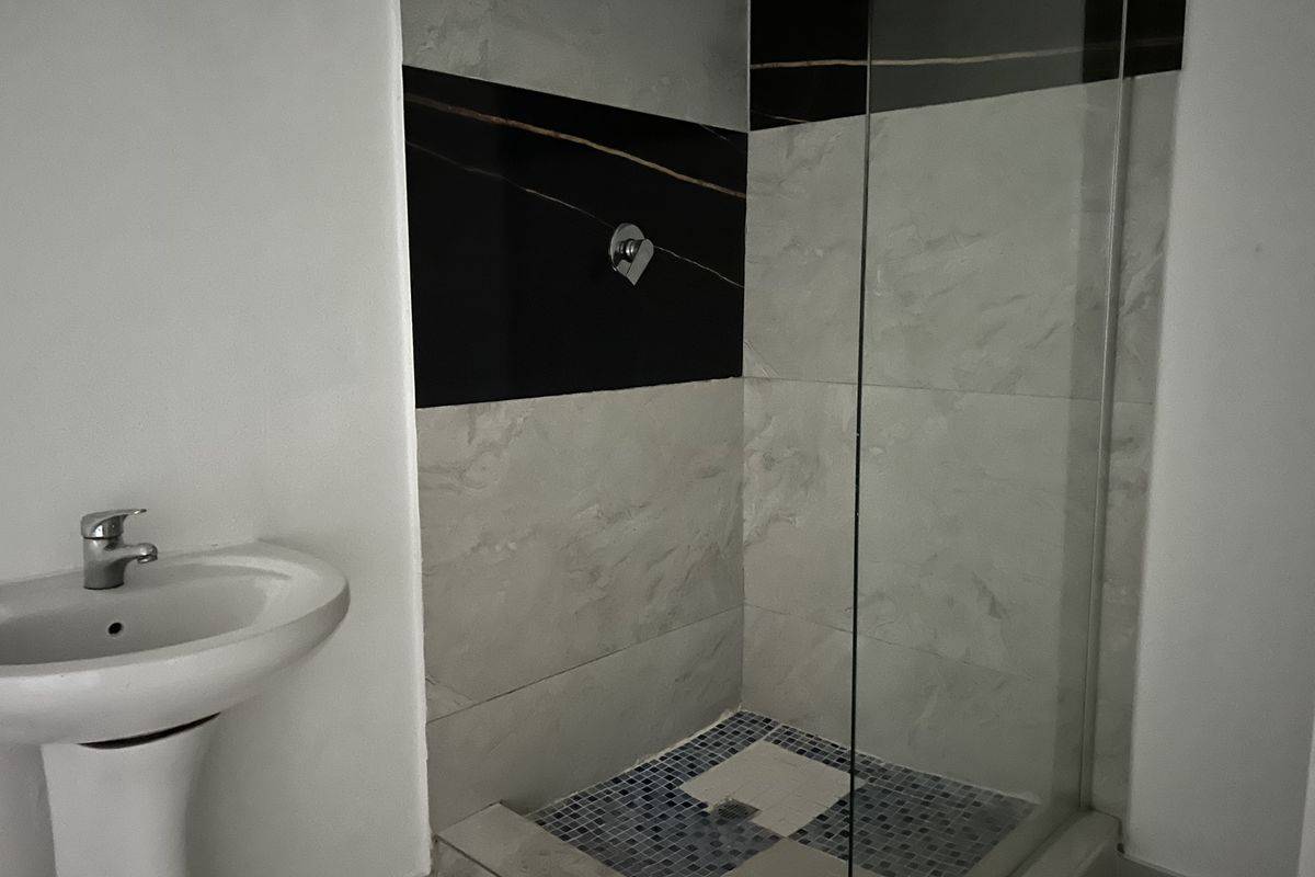 A modern bathroom featuring a pedestal washbasin and a glass-enclosed shower with contrasting black and grey wall tiles.
