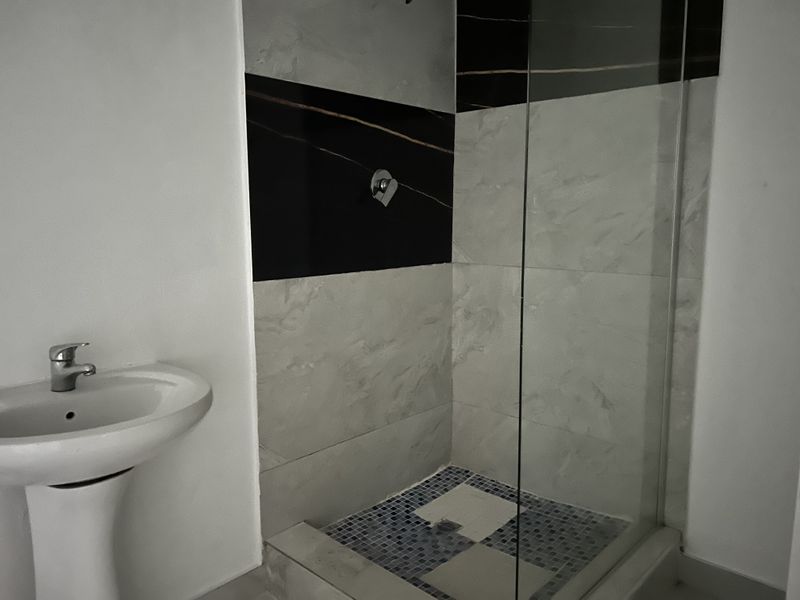 A modern bathroom featuring a pedestal washbasin and a glass-enclosed shower with contrasting black and grey wall tiles.