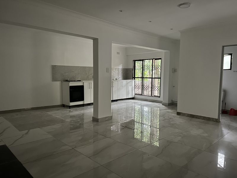 Spacious open-plan living and kitchen area featuring modern tiled flooring, built-in cabinetry, and an integrated oven, offering a bright and versatile living space.