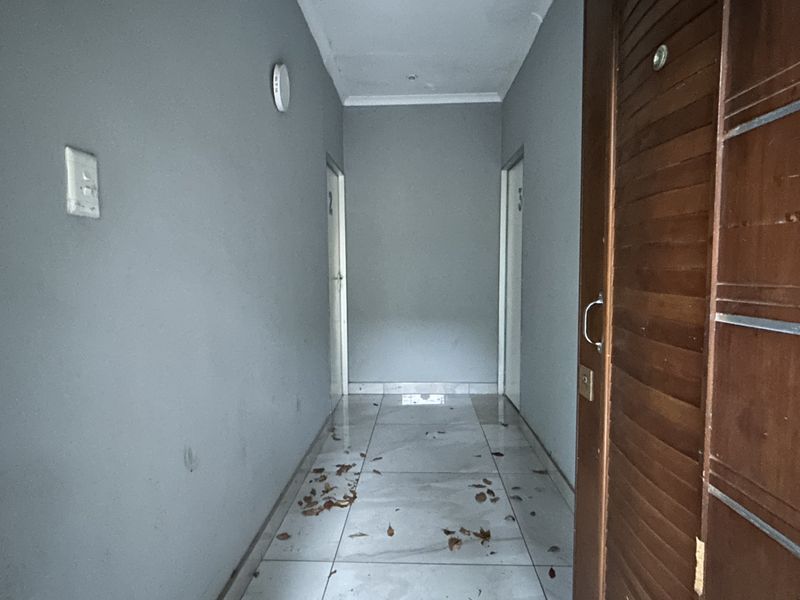 A narrow interior hallway featuring tiled flooring and access to multiple rooms, showing signs of wear and requiring maintenance.