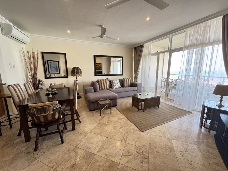 Spacious open-plan living and dining area featuring tiled flooring, ceiling fans, air conditioning, and large sliding glass doors leading to a balcony.