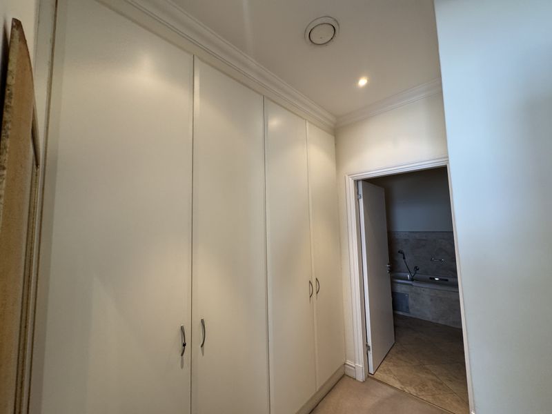 A clean hallway featuring extensive built-in floor-to-ceiling cupboards, recessed lighting, and coving, providing ample storage space and access to an adjoining bathroom.