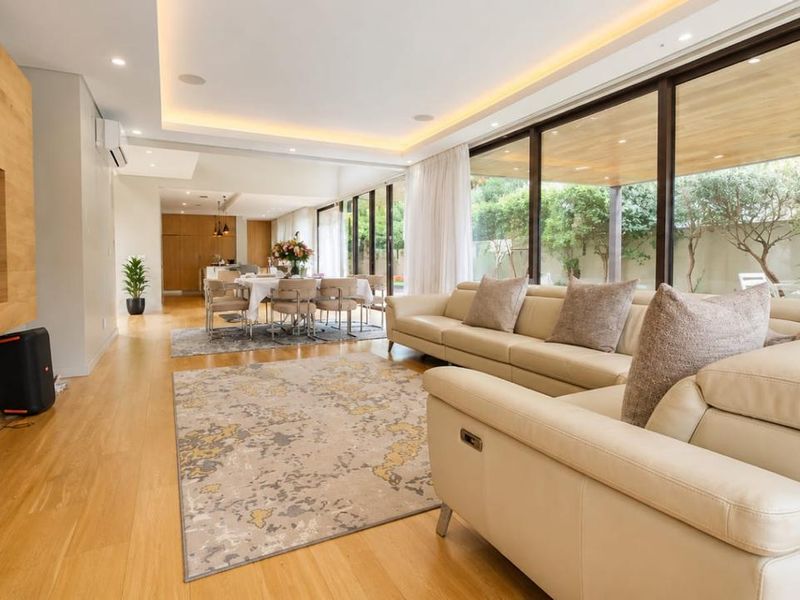 Spacious open-plan living and dining area featuring timber flooring, recessed cove lighting, and expansive floor-to-ceiling glass doors opening to the garden.