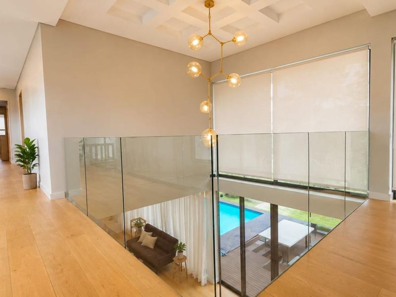 A bright, modern mezzanine hallway featuring high-quality hardwood flooring, a glass balustrade overlooking the lower level, and elegant coffered ceiling details.