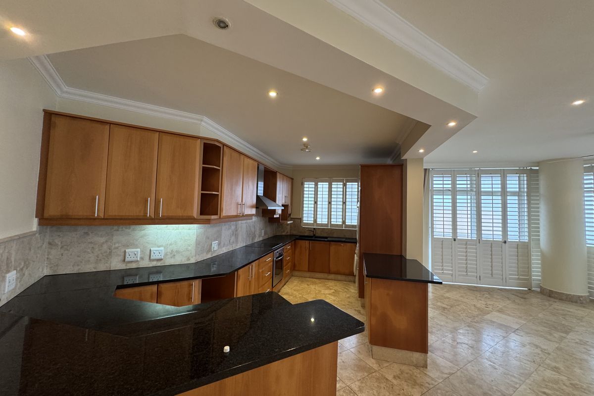 Spacious kitchen featuring wooden cabinetry, granite countertops, built-in oven, extractor fan, and stone flooring, complemented by plantation shutters and recessed lighting.