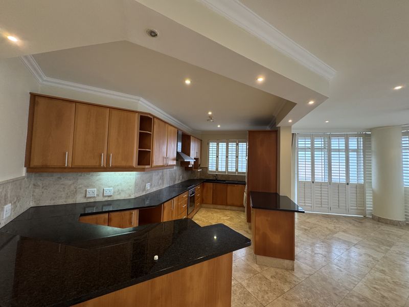 Spacious kitchen featuring wooden cabinetry, granite countertops, built-in oven, extractor fan, and stone flooring, complemented by plantation shutters and recessed lighting.