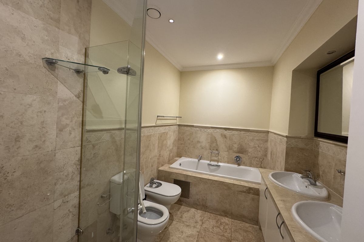 Spacious bathroom featuring a double vanity, built-in bathtub, glass-enclosed shower, bidet, and toilet, finished with elegant travertine tiling throughout.