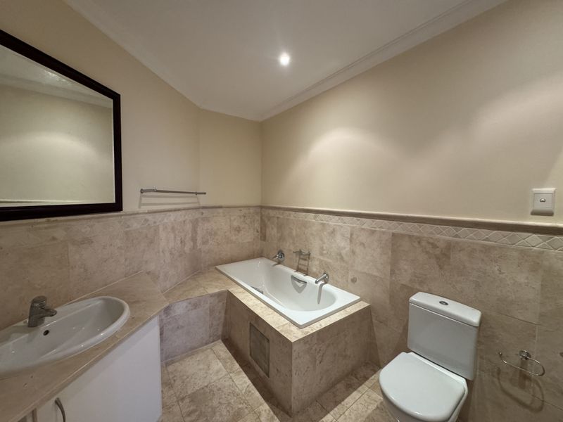 A well-maintained bathroom featuring travertine wall and floor tiles, a built-in bathtub, a vanity basin, and a toilet.