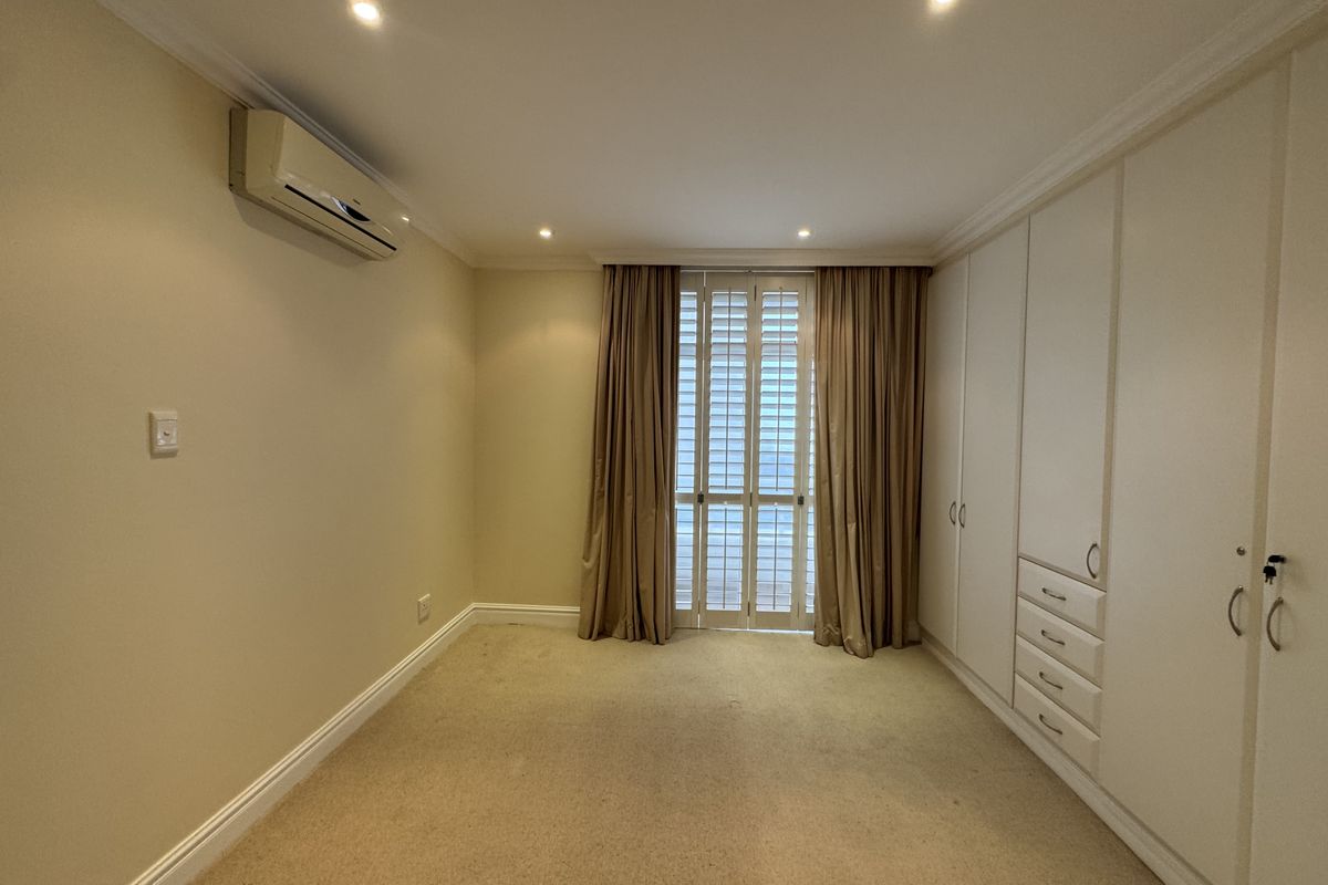 A spacious, empty bedroom featuring neutral carpeting, extensive built-in cabinetry, recessed lighting, and a split-system air conditioning unit.