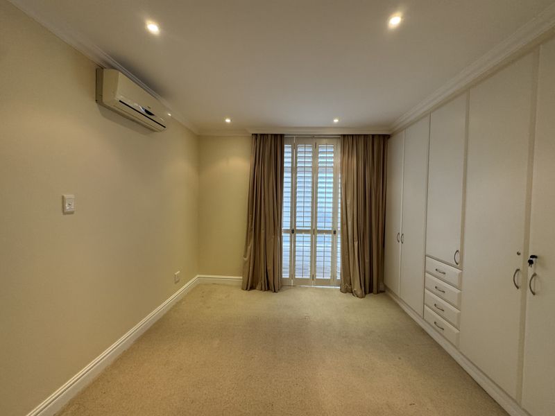 A spacious, empty bedroom featuring neutral carpeting, extensive built-in cabinetry, recessed lighting, and a split-system air conditioning unit.