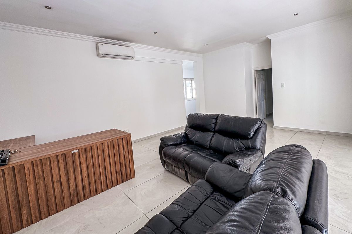 A spacious living room featuring neutral tiled flooring, coved cornicing, recessed downlighting, and a wall-mounted split-system air conditioning unit.