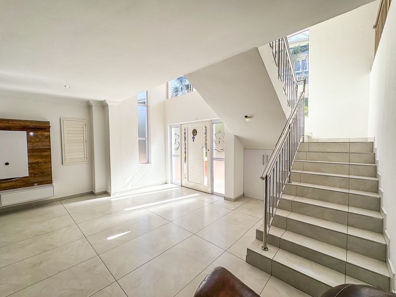 Spacious double-volume entrance hall featuring tiled flooring, a modern staircase with stainless steel balustrades, and built-in storage cabinetry.