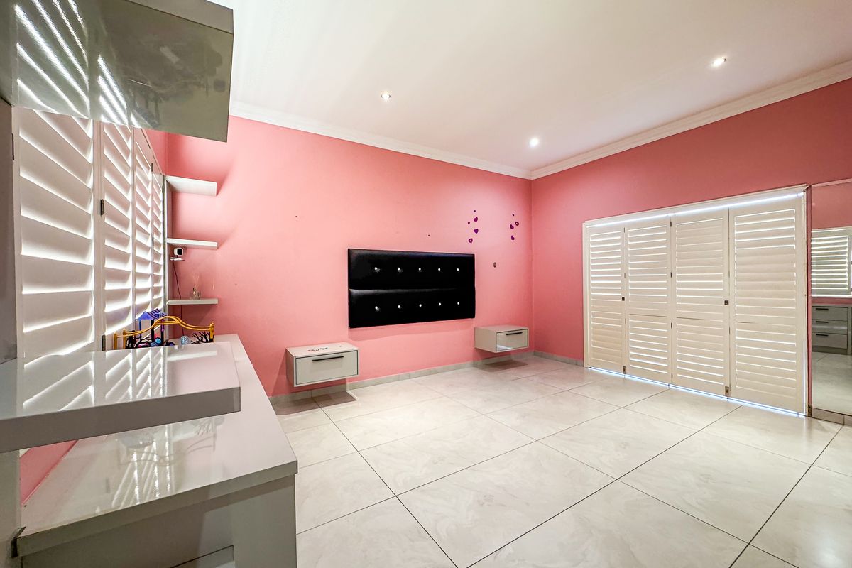 Spacious bedroom featuring large format floor tiles, built-in cabinetry, floating bedside units, and plantation shutters, offering a clean and bright living space.