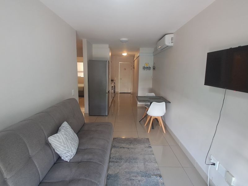An open-plan living area featuring tiled flooring, a wall-mounted air conditioning unit, and recessed ceiling lighting, creating a functional and connected living space.