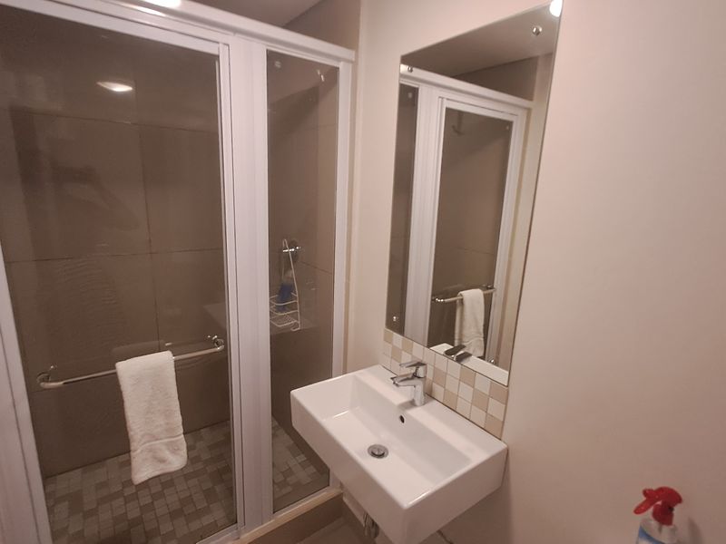A clean, functional bathroom featuring a glass-enclosed shower with tiled finishes and a modern wall-mounted basin with a mirror.
