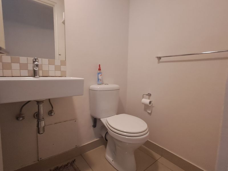 A compact guest bathroom featuring a wall-mounted basin, toilet, and tiled splashback, providing a functional and clean space.
