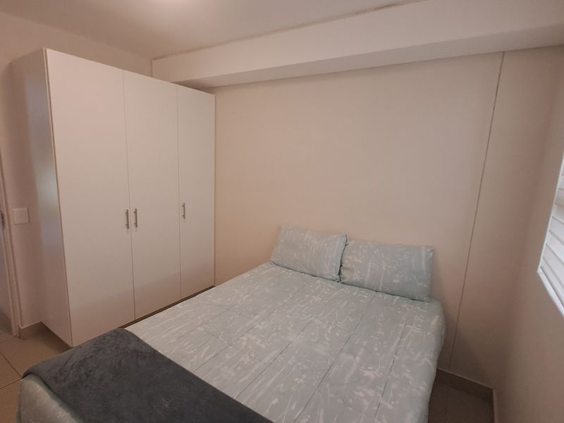 A clean bedroom featuring neutral walls, tiled flooring, a built-in wardrobe, and modern roller blinds, offering a functional and well-maintained living space.