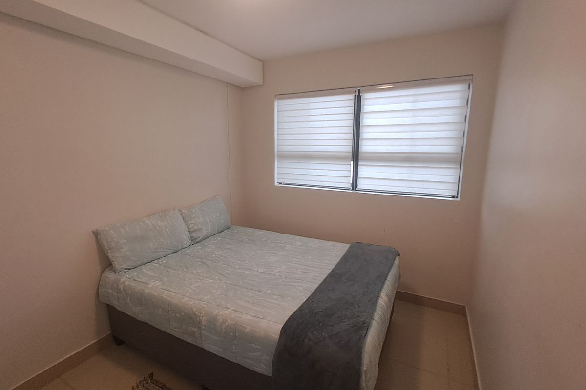 A simple bedroom featuring tiled flooring and modern roller blinds, providing a clean and functional space.