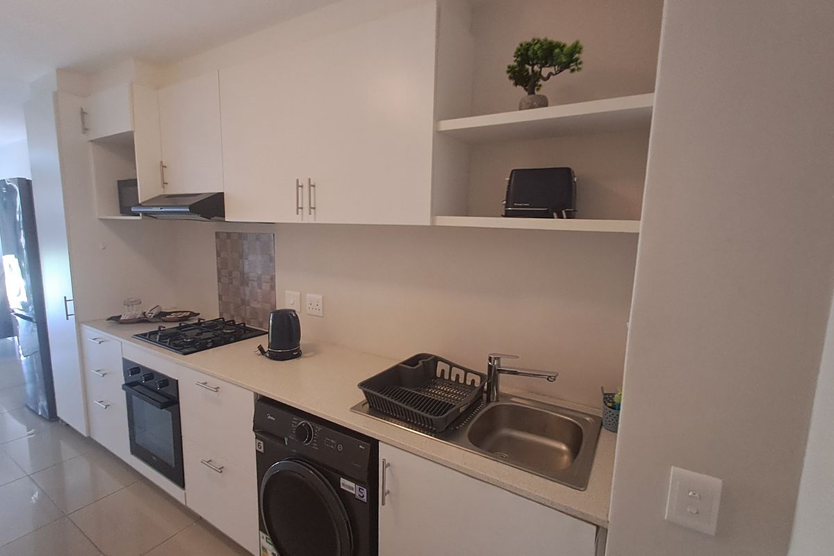 Modern kitchen featuring white cabinetry, stone countertops, gas hob, built-in oven, extractor fan, and an integrated washing machine.
