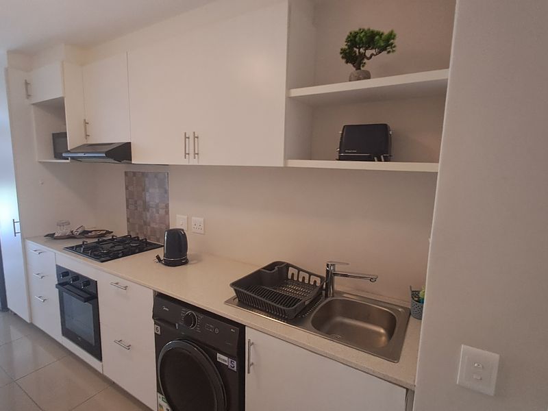 Modern kitchen featuring white cabinetry, stone countertops, gas hob, built-in oven, extractor fan, and an integrated washing machine.