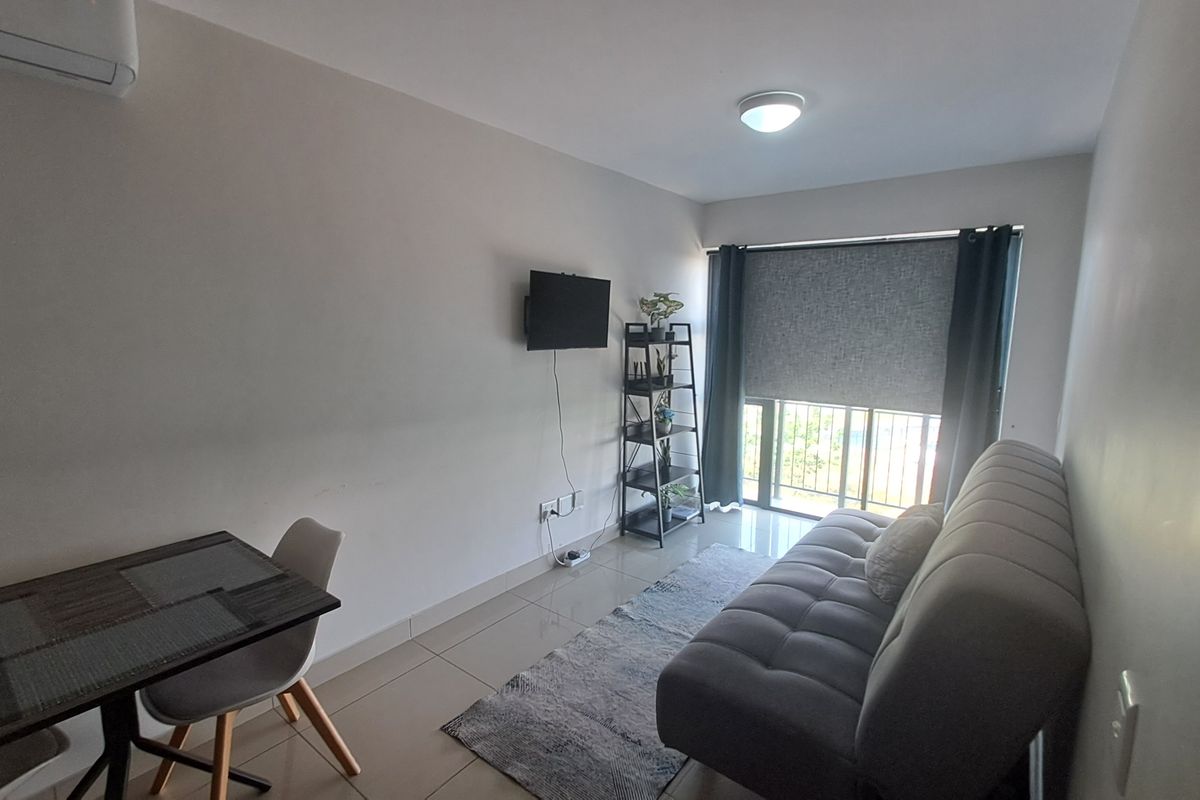 A compact living area featuring tiled flooring, an air conditioning unit, and a sliding glass door with a roller blind and security gate.